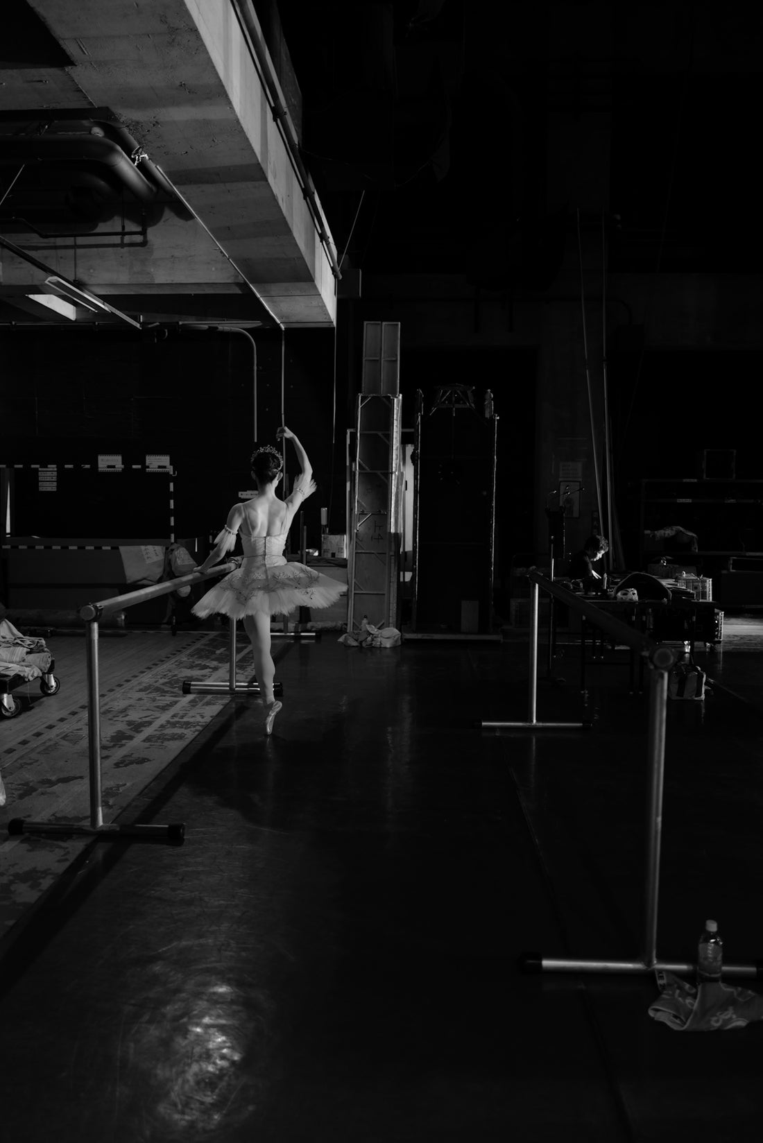 Ballerina practices at a barre in a dimly lit studio.